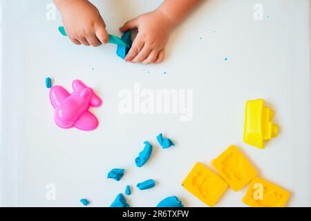 Die Hände eines kleinen Jungen spielen mit blauem Modelton auf weißem Hintergrund. Heimunterricht mit Ton. Draufsicht. Frühentwicklungskonzept Stockfoto