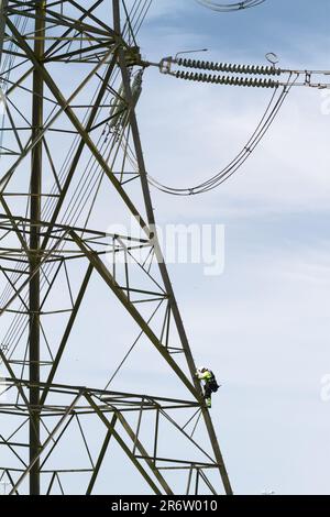 Elektrizitätsarbeiter in Warnjacke und Schutzhelm Klettern auf Einen Metall-Elektrik-Pylon, um ES zu reparieren, England, Großbritannien Stockfoto