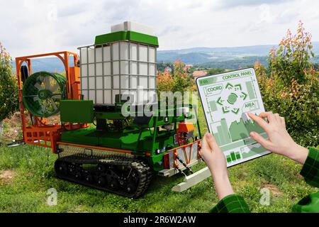 Der Landwirt steuert den autonomen Sprühroboter in einem Obstgarten. Konzept der intelligenten Landwirtschaft Stockfoto