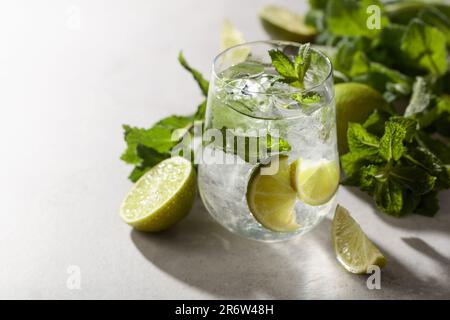 Mojito mit Eis, Limette und Minze auf einem weißen Steintisch. Kühles erfrischendes Getränk mit natürlichem Eis in einem beschlagenen Glas. Stockfoto
