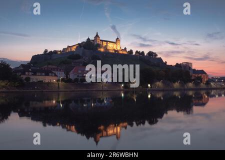 Blick auf das Schloss Marienberg in Würzburg bei Sonnenuntergang mit Reflexion im Flusswasser im Vordergrund. Stockfoto