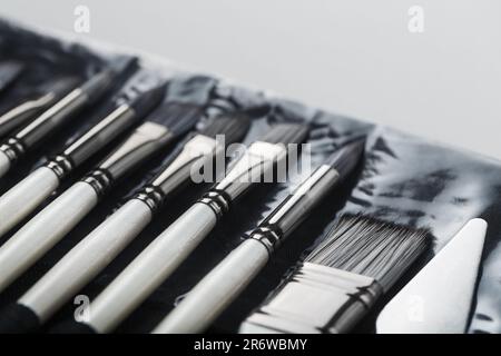 Pinsel, Palettenmesser in einem Federmäppchen auf weißem Leinenhintergrund. Nahaufnahme Stockfoto