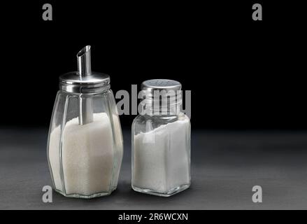 Zuckerspender und Glassalzschüttler auf schwarzem Schieferstein Stockfoto