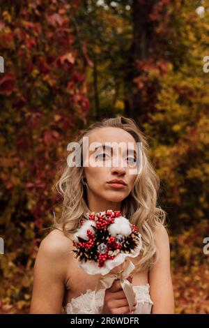 Schöne Braut mit einem Blumenstrauß in der Hand. Hochzeit im Herbst im Wald Stockfoto