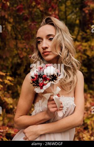 Schöne Braut mit einem Blumenstrauß in der Hand. Hochzeit im Herbst im Wald Stockfoto