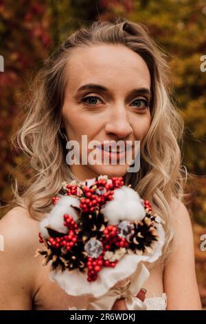 Schöne Braut mit einem Blumenstrauß in der Hand. Hochzeit im Herbst im Wald Stockfoto