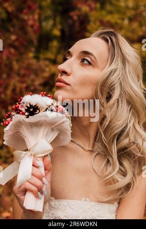 Schöne Braut mit einem Blumenstrauß in der Hand. Hochzeit im Herbst im Wald Stockfoto
