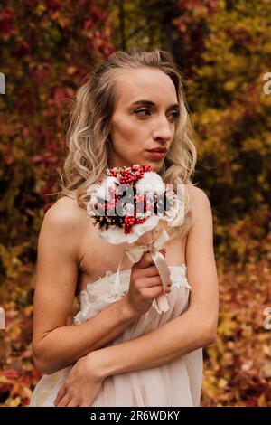 Schöne Braut mit einem Blumenstrauß in der Hand. Hochzeit im Herbst im Wald Stockfoto