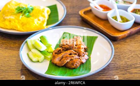 Köstliche asiatische Küche mit zartem geschmortem Fleisch auf Bananenblättern mit geschnittenen frischen Gurken und herzhaften Gewürzen Stockfoto