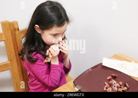 Ein junges Mädchen mit wechselnden Zähnen, das an einem riesigen Schweinerippchen arbeitet Stockfoto