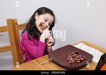 Ein junges Mädchen mit wechselnden Zähnen, das an einem riesigen Schweinerippchen arbeitet Stockfoto