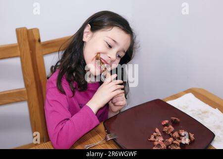 Ein junges Mädchen mit wechselnden Zähnen, das an einem riesigen Schweinerippchen arbeitet Stockfoto