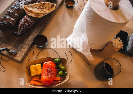 Gegrillte Rippchen mit Gemüse, Rotwein und Servietten. Geräuchertes Schweinefleisch auf Holzbrett und gegrilltes Gemüse. Abendmenü im Restaurant. Stockfoto