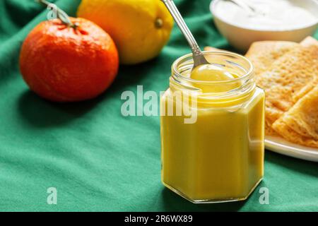 Kurd aus Zitronen und Mandarinen, Pfannkuchen und Sauerrahm auf grünem Hintergrund. Rustikaler Stil. Stockfoto