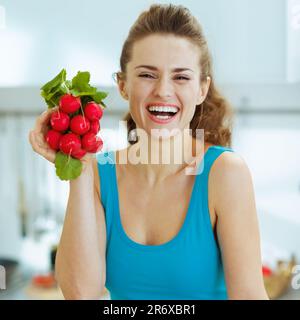 Lächelnde junge Frau mit Bündel Radieschen in Küche Stockfoto