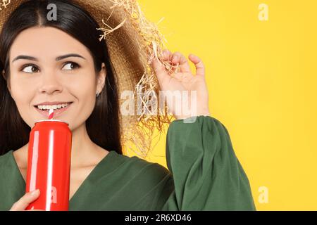 Schöne glückliche Frau, die aus einer roten Getränkedose auf gelbem Hintergrund trinkt. Platz für Text Stockfoto