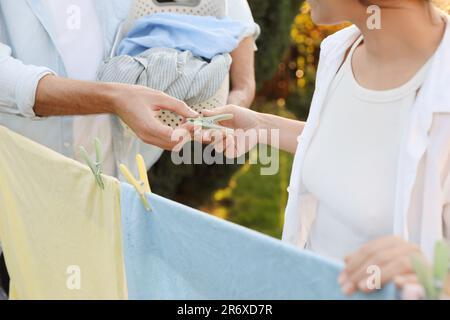 Glückliche Familie, die Kleidung aufhängt, mit Wäscheklammern an der Wäscheleine, zum Trocknen im Garten, Schließung Stockfoto