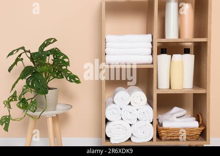 Weiche gefaltete Handtücher und Kosmetikflaschen auf Holzregalen nahe beigefarbener Wand Stockfoto
