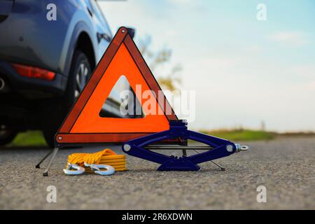 Warndreieck, Abschleppgurt und Scherenheber in der Nähe von Fahrzeugen im Freien. Sicherheitsausrüstung Stockfoto