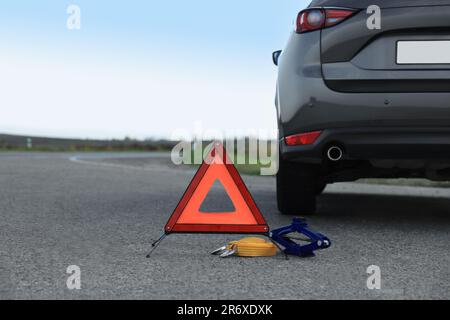 Warndreieck, Abschleppgurt und Scherenheber in der Nähe von Fahrzeugen im Freien. Sicherheitsausrüstung Stockfoto