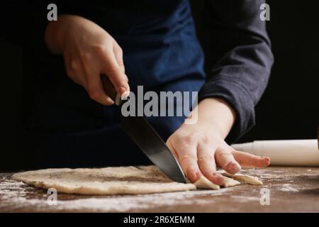 Eine Frau schneidet Teig am Holztisch, Nahaufnahme. Ich koche Grissini Stockfoto