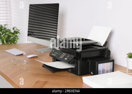 Moderner Drucker mit Papier in der Nähe des Computers auf einem Holztisch im Büro Stockfoto