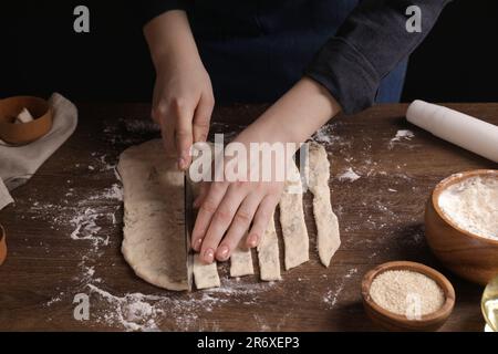 Eine Frau schneidet Teig am Holztisch, Nahaufnahme. Ich koche Grissini Stockfoto