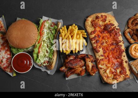 Burger, Pizza und anderes Fast Food auf schwarzem Tisch, flach liegend Stockfoto