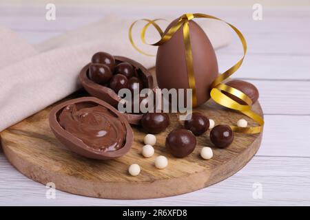 Zusammensetzung mit köstlichen Schokoladeneiern und Süßigkeiten auf weißem Holztisch, Nahaufnahme Stockfoto