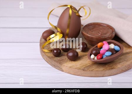 Zusammensetzung mit köstlichen Schokoladeneiern und Süßigkeiten auf einem weißen Holztisch. Platz für Text Stockfoto
