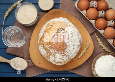 Flache Liegezusammensetzung mit frisch gebackenem Brot und Sauerteig auf blauem Holztisch Stockfoto