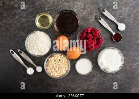 Gesunde Raspberry Muffin Zutaten auf dunklem Hintergrund: Gefrorene Himbeeren, Mehl und andere Zutaten, die verwendet werden, um gesündere Muffins zu machen Stockfoto