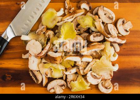 Wildpilze mit einem Küchenmesser auf einem Holzbrett geschnitten: Vorbereitete Austern, Shiitake und Krimini-Pilze, die sich auf einem Schneidebrett stapeln Stockfoto