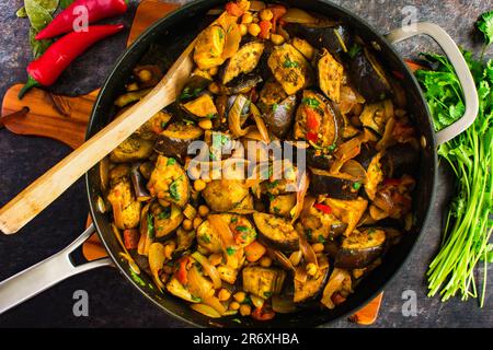 Vegane geröstete Auberginen- und Kichererbsen-Curry serviert in einer Pfanne: Auberginen-Curry mit Garbanzo-Bohnen, Tomaten, Zwiebeln und Koriander Stockfoto