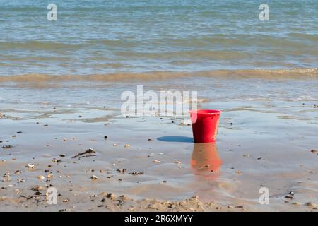 Der rote Strandeimer wurde am Ufer vergessen Stockfoto