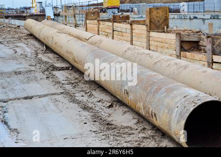 Große Abwasserrohre aus Eisenmetall mit großem Durchmesser für den industriellen Bau von Wasser- oder Abwasserleitungen auf einer Baustelle während der Wiedereinbauphase Stockfoto