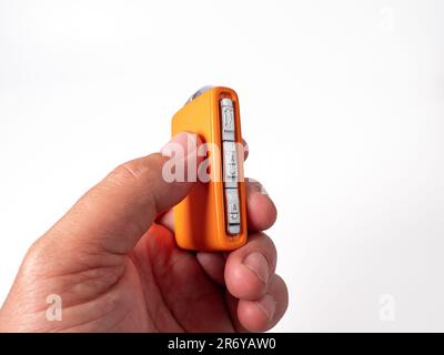 Moderner orangefarbener Funkschlüssel auf weißem Hintergrund in der Hand. Funkschlüssel zum Starten des Motors. Moderne Autoschlüssel. Stockfoto