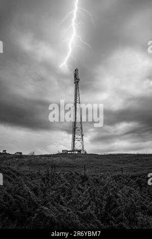 Schwarzweiß-Foto eines Telekommunikationszellen-Turms mit bewölktem Himmel und Blitz Stockfoto