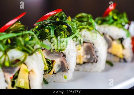 Eine Auswahl an farbenfrohen Sushi-Brötchen, darunter eine California Roll mit Lachs und frischen Produkten, auf weißem Hintergrund. Ein köstliches und gesundes japanisches D Stockfoto