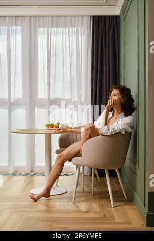 Die junge Barfußfrau sitzt wohlüberlegt mit ihrem Kinn in einem hellen Raum Stockfoto