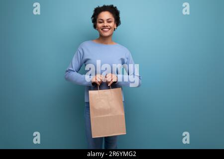 Positive brünette Afro-haarige Frau bekam eine Lieferung in einem Handwerkspaket Stockfoto