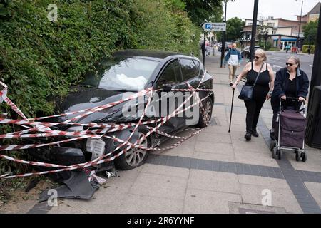 Fußgänger schauen auf ein zerstörtes Fließheckerauto, das auf dem Straßenbelag die Fahrradbarrieren zerdrückte und am 7. Juni 2023 in London in einer städtischen Hecke vor der Harris Academy Schule an der Peckham Road im Süden Londons verbleibt. Stockfoto