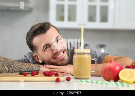 Hübscher Mann mit köstlichem Smoothie und Zutaten am weißen Tisch in der Küche Stockfoto