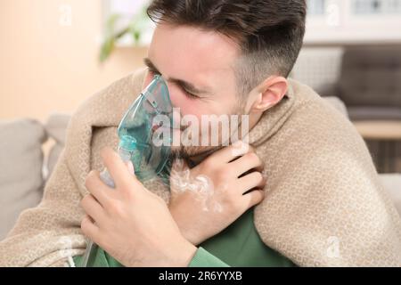 Kranker Mann mit Vernebler zur Inhalation im Innenbereich Stockfoto