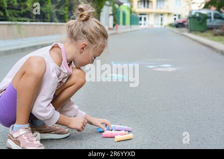 Kleines Kind mit Kreideteilen, das draußen auf Asphalt sitzt, Platz für Text Stockfoto