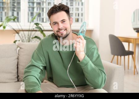 Lächelnder Mann, der zu Hause einen Vernebler zur Inhalation auf dem Sofa hält Stockfoto