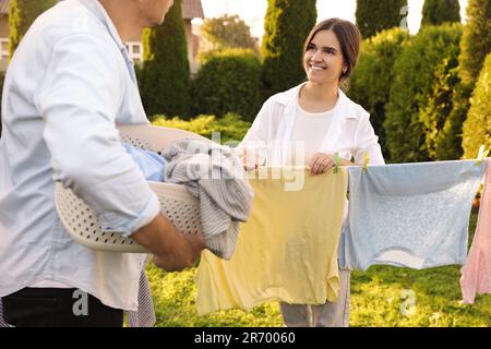 Glückliche Familie, die Kleidung aufhängt, mit Wäscheklammern an der Wäscheleine, um im Garten zu trocknen Stockfoto