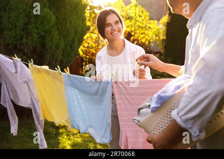 Glückliche Familie, die Kleidung aufhängt, mit Wäscheklammern an der Wäscheleine, um im Garten zu trocknen Stockfoto
