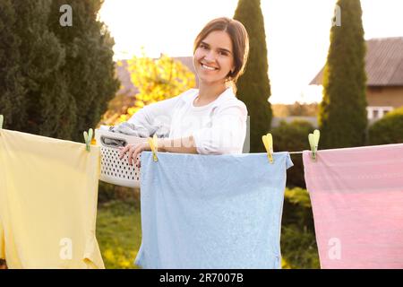 Frau mit Korb trocknet Kleidung im Garten an sonnigen Tagen Stockfoto