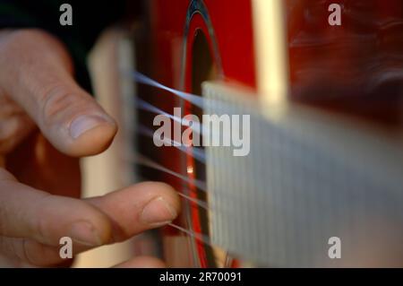 Ein Detailfoto von einem mann Finger und Saiten einer Gitarre, die gespielt wird. Stockfoto